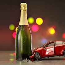 Wie viel Promille liegen drin? Symbolisches Bild in welchem ein Spielzeugauto in eine Sektflasche kracht
