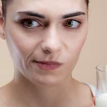Wenn Milch Bauchweh macht Eine Frau mit einem Glas Milch in der Hand schaut skeptisch.