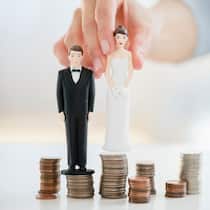 Wann ist Gütertrennung sinnvoll? Zwei Figuren einer Braut und eines Bräutigams werden auf einen Stapel Geldmünzen gesetzt, die voneinander getrennt sind.