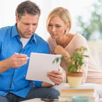 Ich habs mir anders überlegt! Ein Paar sitzt auf einem Sofa im Wohnzimmer, der Mann hält einen Vertrag in seinen Händen und schaut sich diesen zusammen mit seiner Partnerin an.