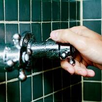 Die Gefahr lauert im Badezimmer Hand dreht in der Dusche den Hahn auf. Unvorsichtiges Energiesparen kann zu Legionellen im Duschwasser führen.