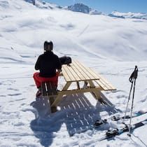 Was gilt bei der Skimiete? Skifahrer sitzt auf einem Bank an einem Tisch neben der Skipiste.