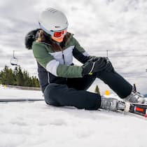 Wer zahlt bei einem Skiunfall im Ausland? Eine Skifahrerin hält sich nach einem Sturz das Knie und liegt auf dem Boden. Zahlt die Versicherung bei einem Skiunfall und wie sieht es aus, wenn der Unfall im Ausland passiert?