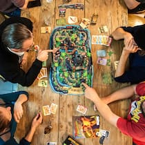 Gesellschaftsspiele boomen wie nie Vier Spielerinnen und Spieler spielen ein Gesellschaftsspiel am Tisch