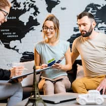 Darf das Reisebüro Gebühren verrechnen? Eine Angestellte eines Reisebüros berät ein junges reisewilliges Paar.