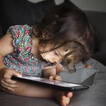 Das Kleinkind mit dem Tablet beruhigen? Tun Sie das nicht! Kleines Mädchen starrt auf ein Handy - Handys und Tablets faszinieren schon die Kleinsten, können aber ihre Entwicklung gefährden. Neue Empfehlungen des Marie Meierhofer Instituts für das Kind zeigen, wie Eltern Risiken minimieren und Chancen nutzen können
