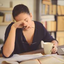 So meistern Sie die Arbeit zu Hause Junge Frau sitzt zu Hause am Tisch und arbeitet. Sie hat den Kopf aufgestützt. Sie schaut traurig und gelangweilt.