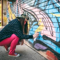 Mit diesen Strafen müssen Jugendliche rechnen Junge Frau mit Bandana sprayt ein Graffiti an eine Wand