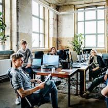Das Büro ist tot – es lebe das Büro Eine Gruppe casual gekleideter Geschäftsleute steht und sitzt für ein Meeting zusammen.