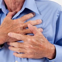 Was fehlt dir, mein Herz? Senior adult man clutching his chest in pain. Heart attack, heart disease. He wears a medical alert bracelet and blue dress shirt.