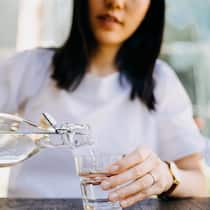 Wasser trinken hilft beim Abnehmen Eine Frau schenkt sich ein Glas Wasser ein.