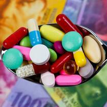 Die Alibiübung der Pharmaindustrie Jemand hält einen Löffel voll Tabletten über ein paar Schweizer Banknoten.