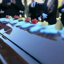 Steuererklärung für Verstorbenen ausfüllen Sarg an Beerdingung auf dem Friedhof und es stehen einige Trauergäste rund herum.