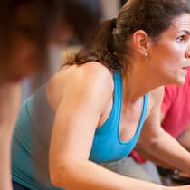 Erste Schritte für Sportmuffel Eine Frau trainiert im Fitnesscenter mit einer Gruppe auf dem Fahrrad.