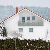 Wie werde ich Vermieterin? Ein Einfamilienhaus auf dem Land, umgeben von verschneiten Wäldern.