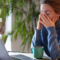 Darf ich im Homeoffice einen zweiten Job annehmen? Eine Frau sitzt zu Hause am Laptop und reibt sich die Augen
