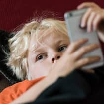 Kind ist sehr minimalistisch – wie sollen Eltern reagieren? Ein junger Teenager-Junge liegt auf dem Sofa und hat ein Handy in der Hand