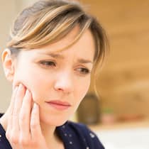 Zahn abgebrochen – zahlt die Versicherung? Eine Frau mit Zahnschmerzen hält sich die Wange