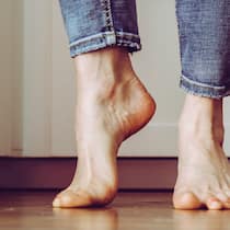 Diese Übungen helfen gegen Fussschmerzen Ein Mann steht mit nackten Füssen auf den Zehenspitzen