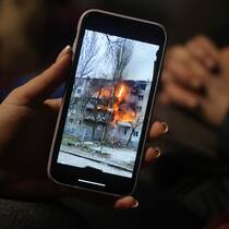 Wie mit Schwierigkeiten umgehen? Eine Frau betrachtet auf ihrem Handy ein Bild von einem bombardierten Gebäude in der Ukraine