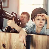 Kind will Krieg spielen – wie sollen Eltern reagieren? Zwei junge Buben spielen Soldaten in der Stube mit Spielzeugwaffen