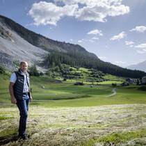 Wenn das Haus in einer Gefahrenzone steht Gemeindepräsident von Brienz, Daniel Albertin, steht auf einer gemähten Wiese, im Hintergrund ist abgerutschtes Geröll erkennbar.