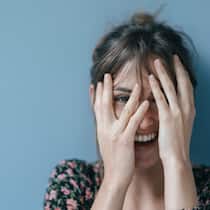 Wer lacht, lebt leichter Eine Frau lacht und bedeckt dabei ihr Gesicht teilweise mit ihren Händen