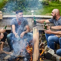 Wie reagieren bei frauenfeindlichen Sprüchen? Vier Männer sitzen draussen an einem Feuer, trinken Bier und lachen