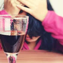 Wenn Rotwein für rote Köpfe sorgt Eine Frau sitzt vor einem Glas Rotwein und hält sich den Kopf