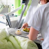So tricksen Krankenkassen mit dem Austrittstag Pflegerin an Spitalbett mit Essen