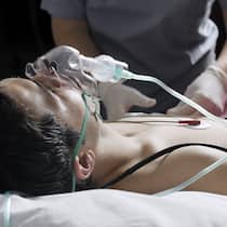 Checkliste für Ihre Patientenverfügung Ein Mann mit einer Sauerstoffmaske liegt in einem Bett und wird von einer Person mit Handschuhen betreut.