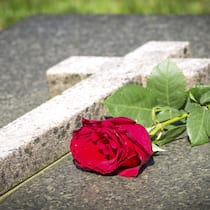 Was nach einem Todesfall getan werden muss steinernes Grab mit einem Kreuz, auf dem eine rote Rose liegt