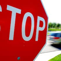 Welche Busse droht? Stop-Schild im Vordergrund, vorbeifahrendes Auto im Hintergrund