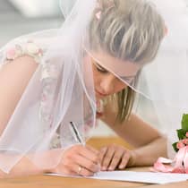 Wer trägt nach der Hochzeit welchen Namen? Eine Frau in weissem Brautkleid setzt ihre Unterschrift auf ein Dokument zur Eheschliessung.