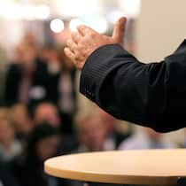 So wird die Generalversammlung ein Erfolg Mann in Anzug vor Versammlung Fokus auf linkem Arm, der leicht angehoben ist