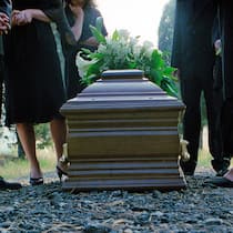 Drei typische Irrtümer Mit Blumen geschmückter Holzsarg an Trauerfeier und Trauergäste stehen um den Sarg herum.