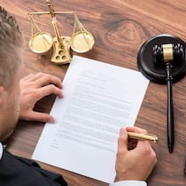 Wann lohnt sich eine Einsprache? Ein Mann füllt ein Formular aus, das neben einem Richterhammer und einer Waagschale für Gerechtigkeit liegt. In welchen Fällen lohnt es sich, Einsprache gegen einen Strafbefehl zu erheben?