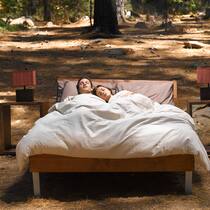 Vormieter blockiert Wohnung – was tun? Ein Pärchen schlaft in ihrem Bett, das in einem Wald steht.