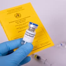 Wenig Transparenz beim digitalen Impfausweis Eine medizinische Person hält einen Papier-Impfausweis und den Impfstoff in der Hand.