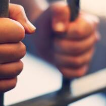 Ein Leben hinter Gittern Hände, die ein Gefängnisgitter festhalten