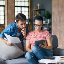 So füllen Sie Beitragslücken in Ihrer Vorsorge am sinnvollsten auf Couple calculating bills at home using laptop and calculator. Young couple working on computer while calculating finances sitting on couch. Young man with wife at home analyzing their finance with documents.1414921475