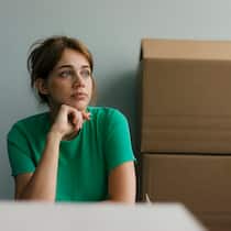 Wer die Miete nicht zahlt, fliegt raus Mieterin sitzt neben ihren Umzugskartons und schaut traurig.