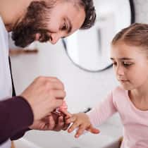 Alternierende Obhut – wie teilen wir den Unterhalt fair? Ein kleines Mädchen hat ihre rechte Hand ausgestreckt, damit ihr Vater die Nägel lackieren kann.