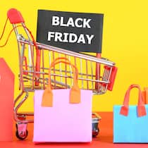 So sparen Sie bei der Black-Friday-Sause wirklich Ein Einkaufswagen mit Einkaufstaschen, Sale-Schild und Black-Friday-Aufschrift vor gelbem Hintergrund. Wie man an Black Friday wirklich spart