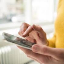 8 Tipps für kürzere Ladezeiten Eine Frau, deren Gesicht man nicht sieht, und die einen gelben Pullover trägt, tippt auf den Bildschirm eines Smartphones.