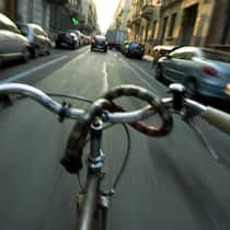 Velofahren mit Schwips – darf ich das? Eine Velofahrer rast durch eine Strasse, an deren Seiten Autos parkiert sind und die aus Sicht des Fahrradfahrers etwas verschwummen aussehen - Was gilt in der Schweiz, wenn man nach dem Genuss von Alkohol betrunken mit dem Velo fährt? Der Beobachter zeigt, welche Konsequenzen dies hat.