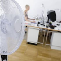 Wer muss den Büro-Ventilator bezahlen? Ein Ventilator ist in einem Büro vor zwei Arbeitstischen aufgestellt - Was können Angestellte in der Schweiz verlangen, wenn es im Büro zu heiss ist? Der Beobachter zeigt, was der Gesundheitsschutz dazu sagt.