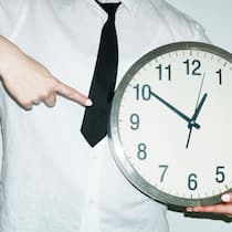 Zürcher Start-up fordert 100-Stunden-Woche – das gilt beim Arbeitsrecht Person wearing office work shirt and tie holding and pointing a clock with hard direct flash