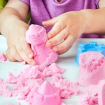 Wo die tödlichen Fasern lauern Child's hands building sand castle from pink kinetic sand on the white table; selective focus