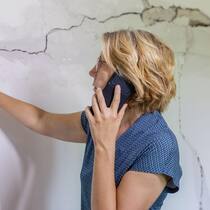 Wer zahlt den Schaden durch ein Erdbeben? Eine Frau begutachtet die Schäden und Risse in der Hausmauer und meldet diese telefonisch der Versicherung. Wenn in der Schweiz die Erde bebt, stellt sich die Frage, welche Versicherung kommt für allfällige Schäden auf. So gestaltet sich die Situation in den Kantonen.